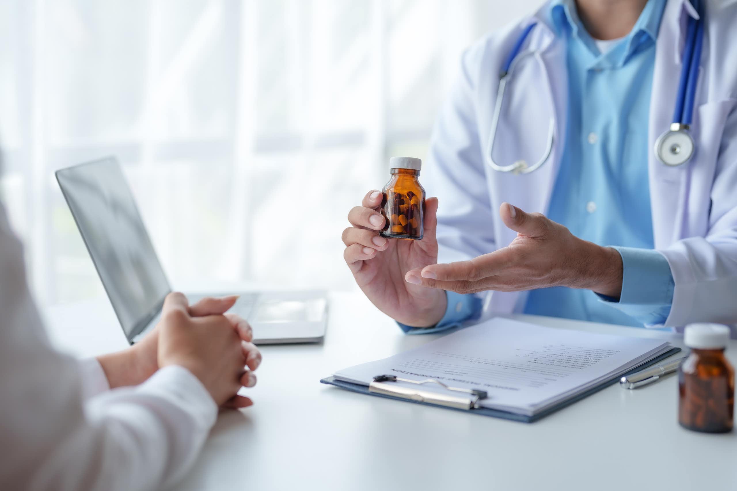 Un médecin est face à un patient en pleine discussion. Il tient un flacon de pilules à la main.