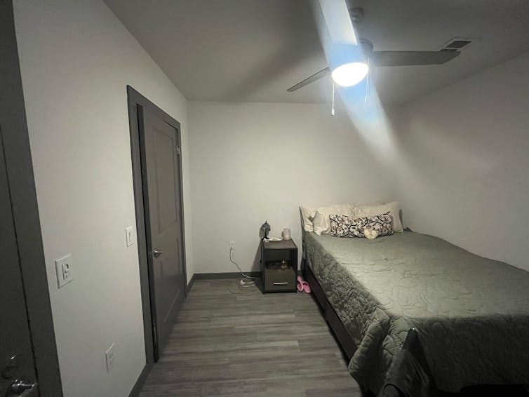 A bed and nightstand in a windowless room with a ceiling fan.