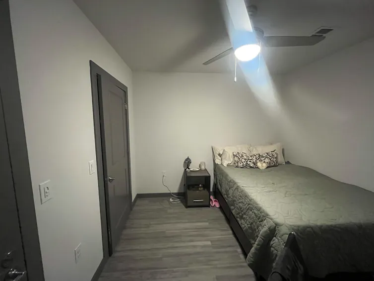 A bed and nightstand in a windowless room with a ceiling fan.
