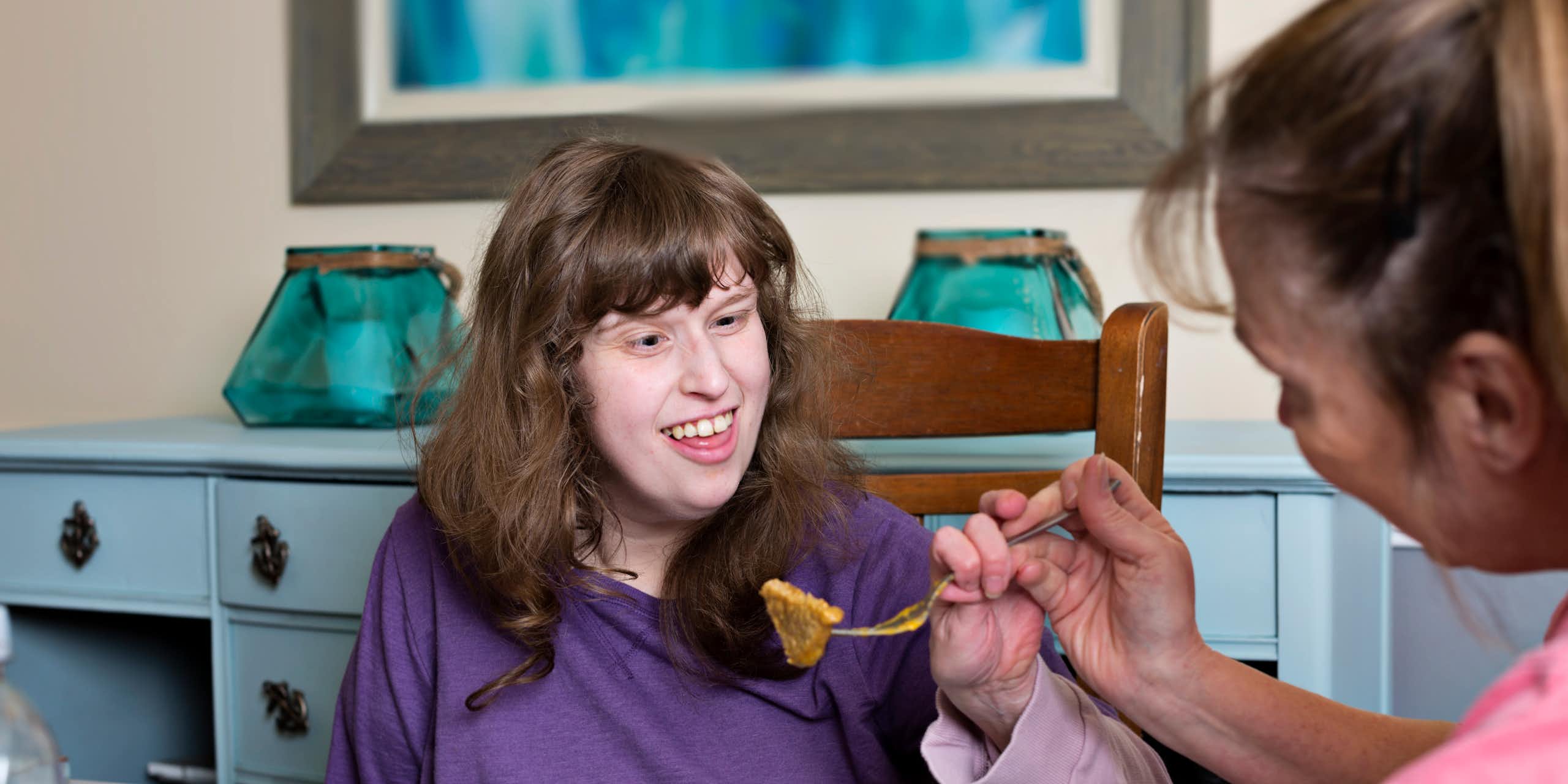 Disabled young woman is assisted to use her fork to eat dinner.