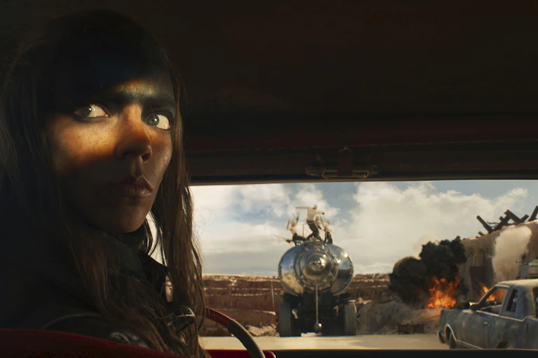 A person's illuminated eyes seen in a dark vehicle with an explosion out the window.