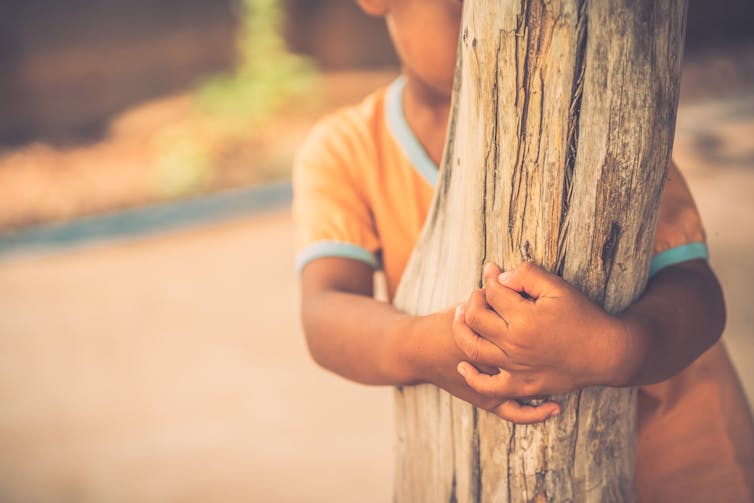 A shy child hiding behind a tree
