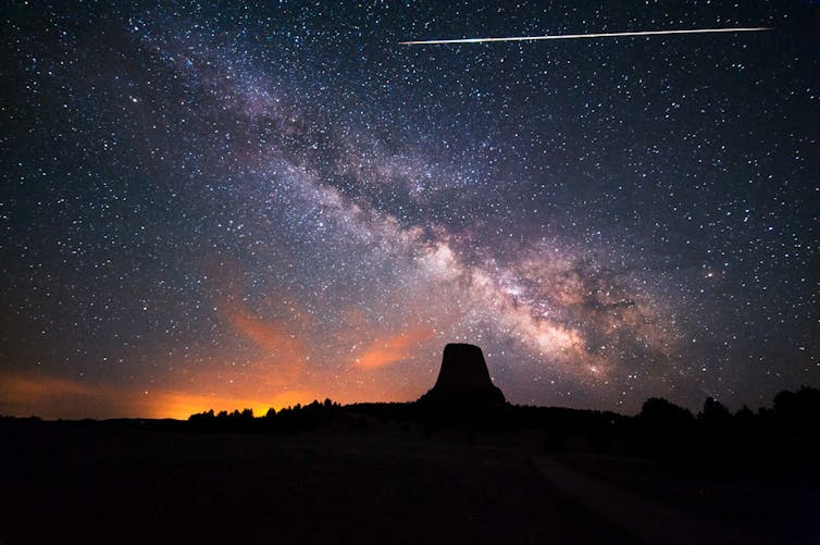 A long exposure night sky with milky way, red sunset and a bright streak clearly visible.