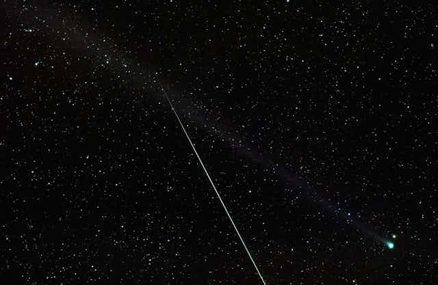 A meteor streaks through a photograph of a green comet.