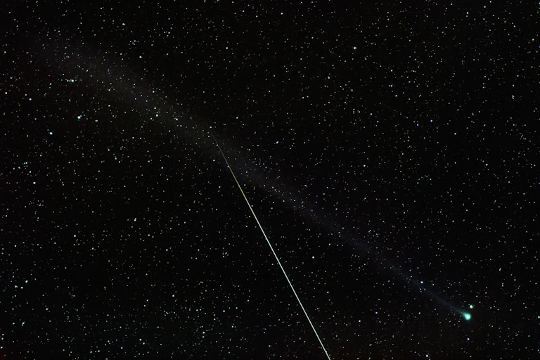 A meteor streaks through a photograph of a green comet.