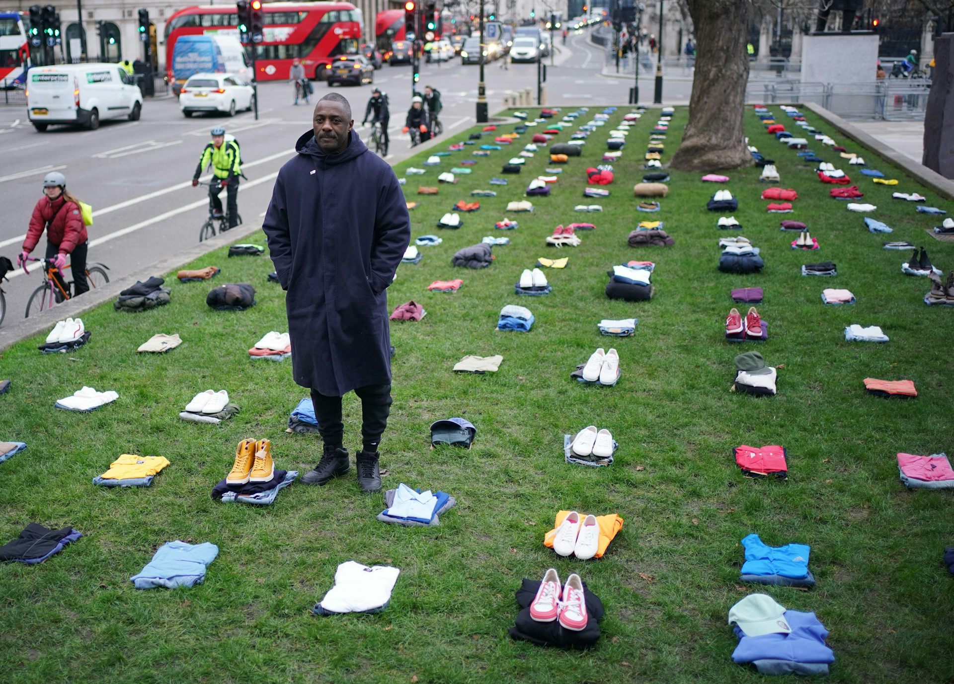 A man stands on a green surrounded by piles of neatly folded clothes.