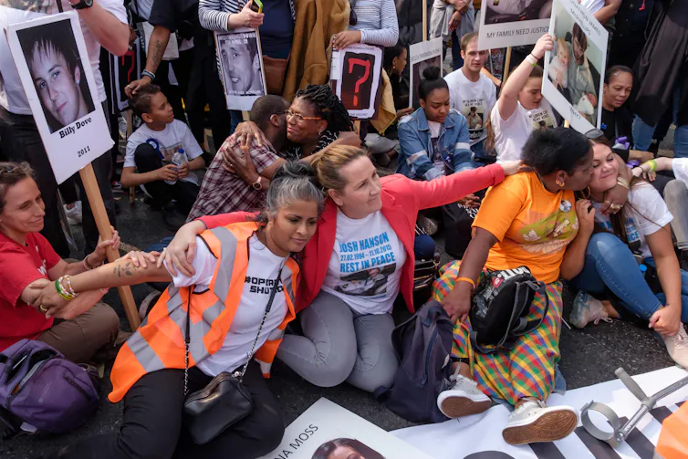 Protestors sit on the pavement with hi-vis vests and placards.