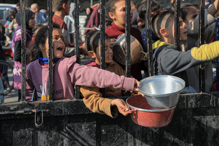 Children carry pots and pans as they queue for aid in trhe Gaza Strip, February 2024.