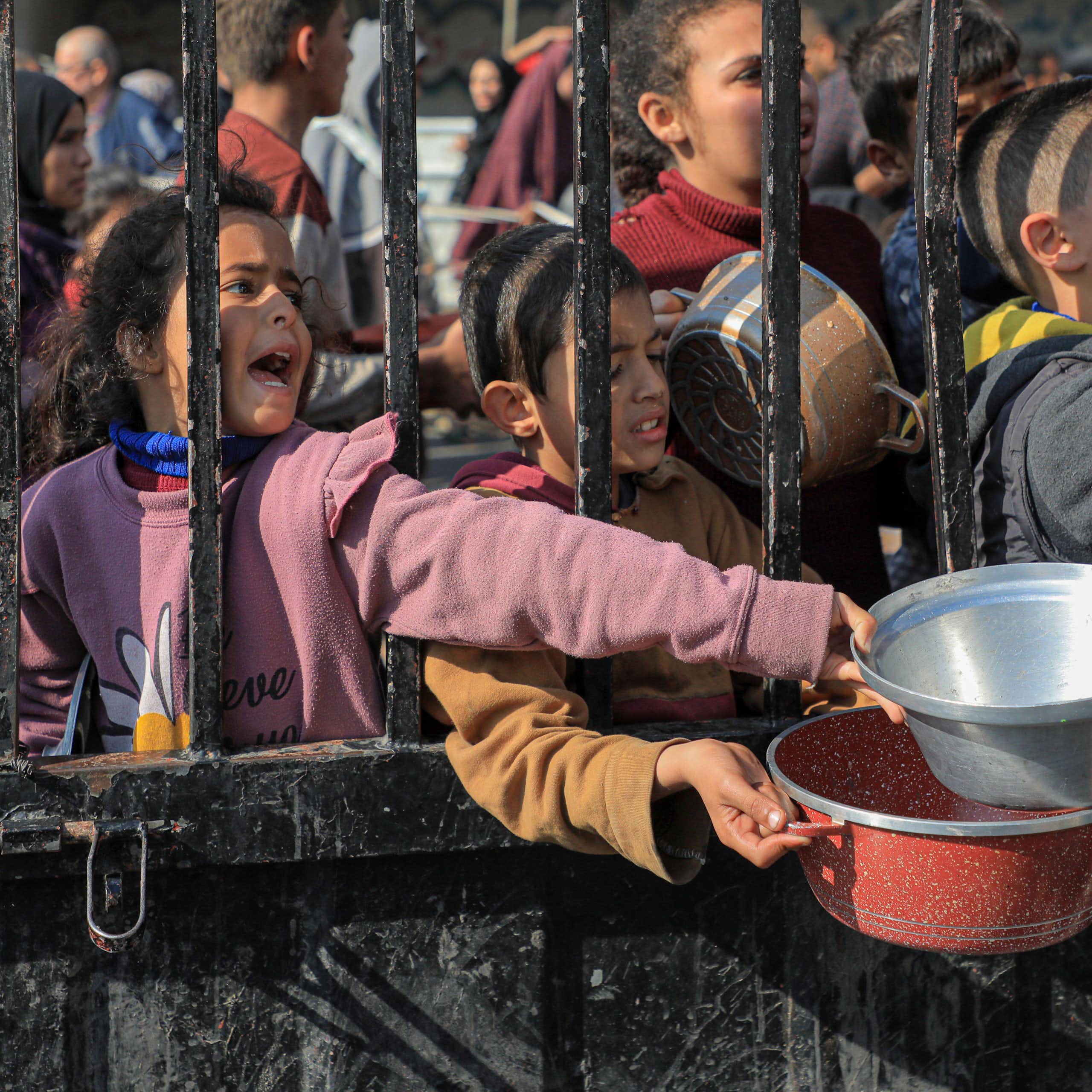 Children carry pots and pans as they queue for aid in trhe Gaza Strip, February 2024.