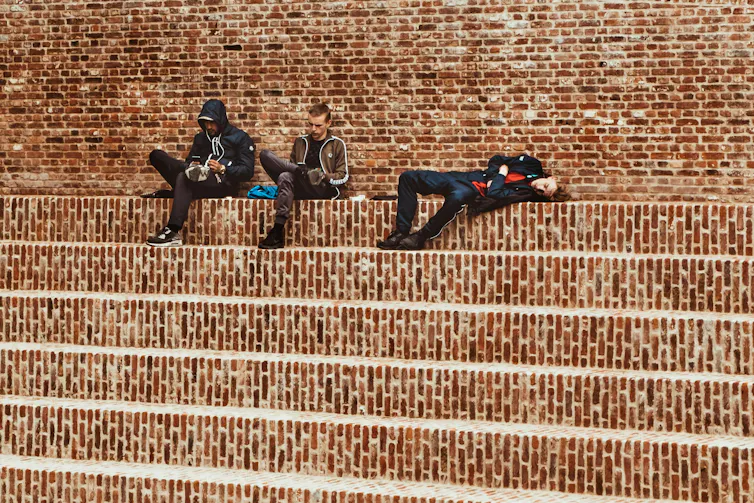 People looking at their phones against a brick background.