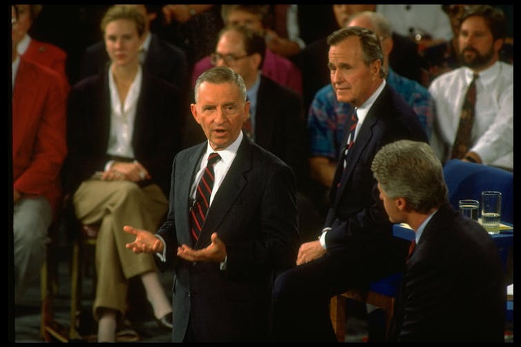 Three men in suits talking with each other while standing.