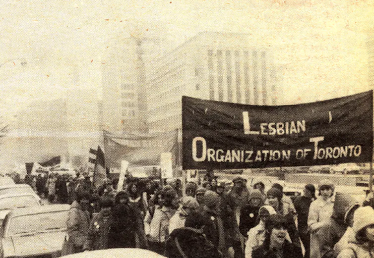 A black and white photo of people at a demonstration carrying a large banner reading: Lesbian organization of Toronto.
