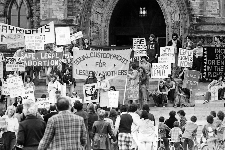A black and white photo of people at a demonstration with signs calling for equal rights for LGBT people