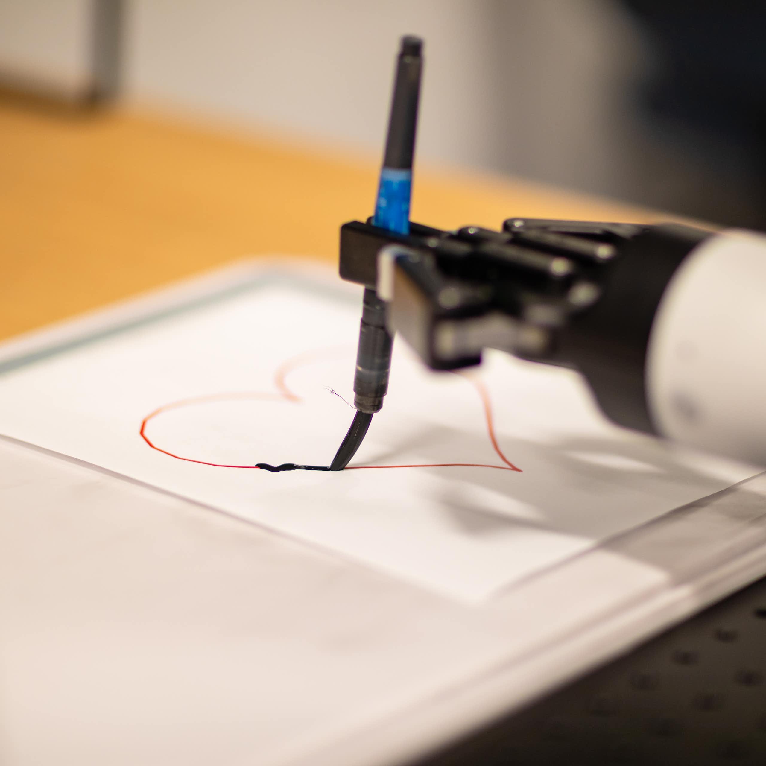 a robot hand holds a paint brush tracing a heart on a piece of paper