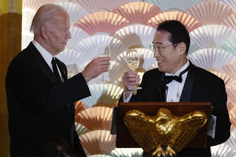 Two men in black-tie suits toast with wine glasses.