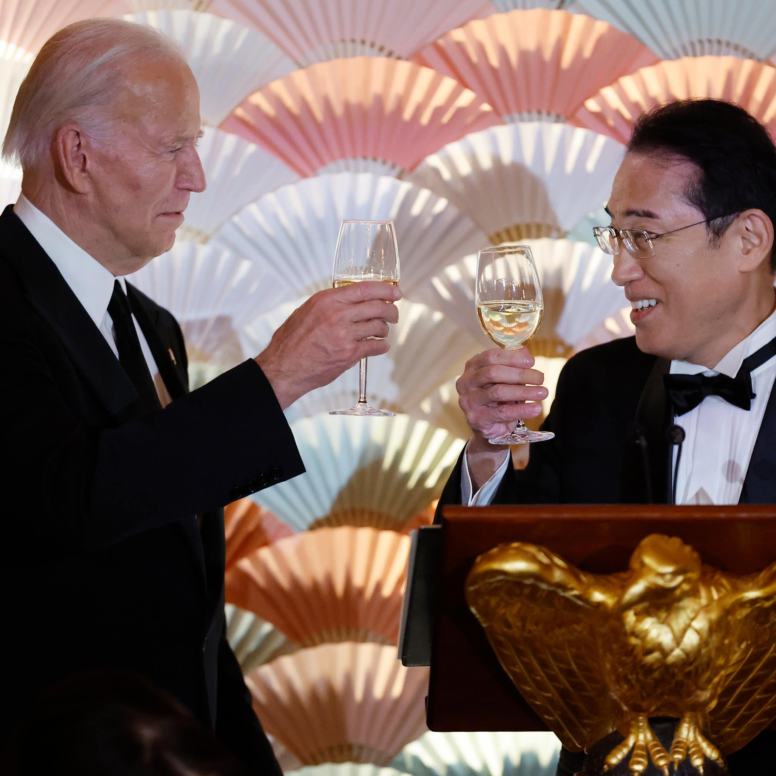 Two men in black-tie suits toast with wine glasses.