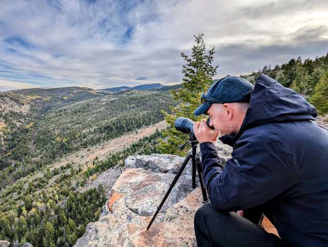 Man looking through binoculars on rock over big wide mountain landscape