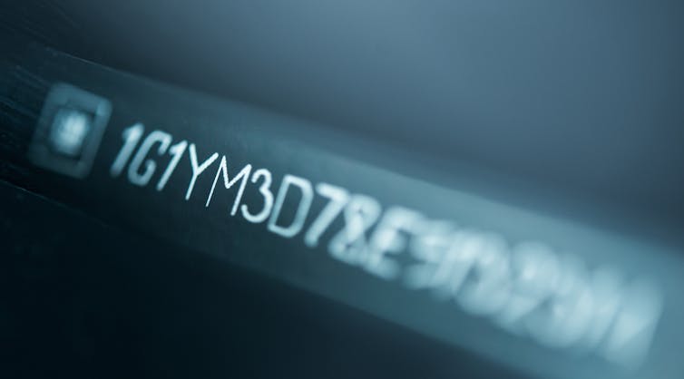 A series of letters and numbers that make up a VIN are written in white on a grey background. The numbers blur at the edges.