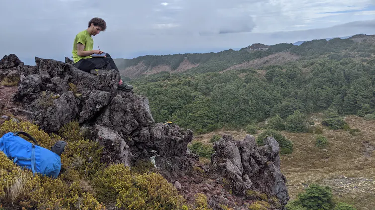 Scientist sitting on an outcrop, recording notes about a rock sample