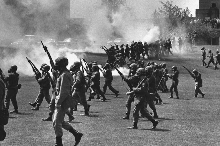A black and white photo shows armed soldiers marching on a student protest.