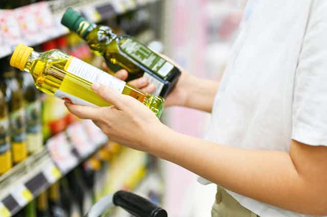 Woman in supermarket comparing two small bottles of oil, one olive oil