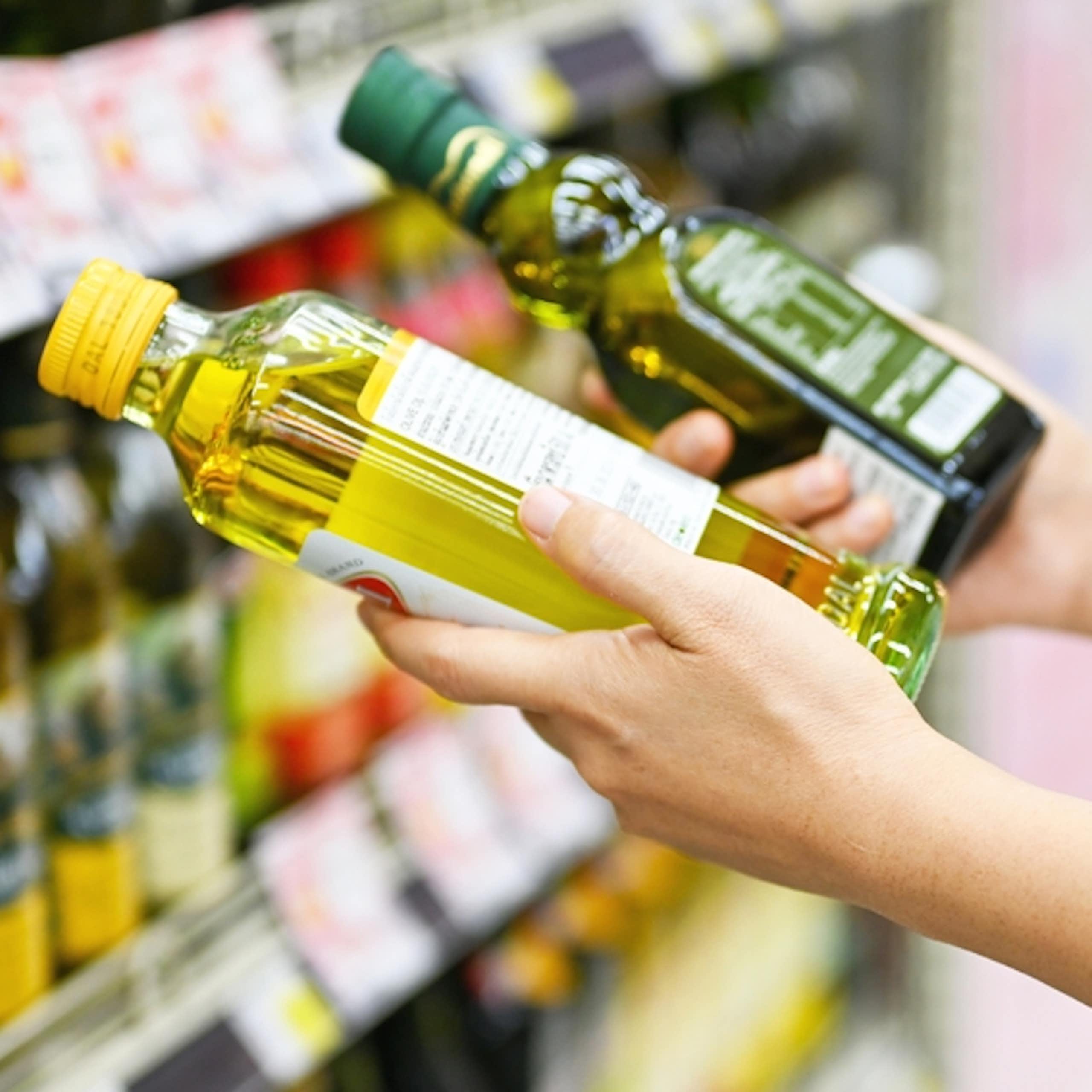 Woman in supermarket comparing two small bottles of oil, one olive oil