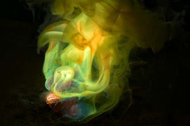 Photo of glowing greenish-yellow chemicals swirling against a dark background.