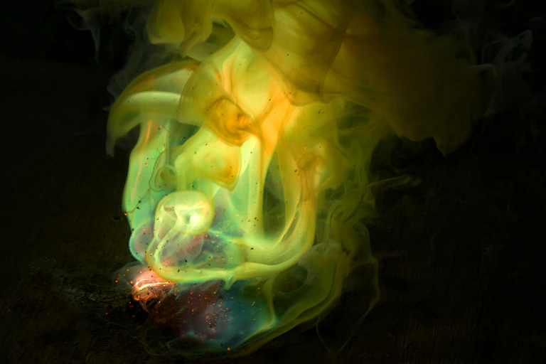 Photo of glowing greenish-yellow chemicals swirling against a dark background.