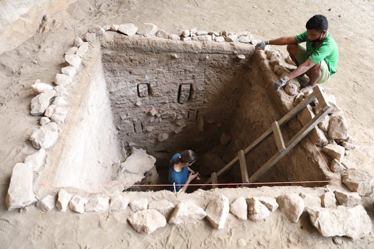 Photo of two people with a neat square pit dug in a a dirt surface.