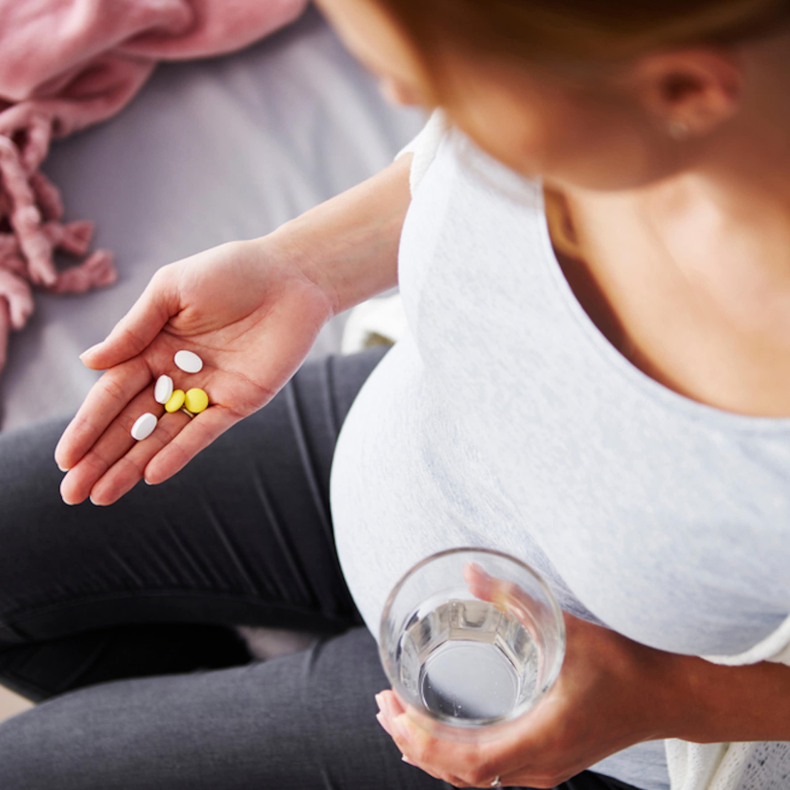 Pregnant woman holding glass water in one hand, supplements in other