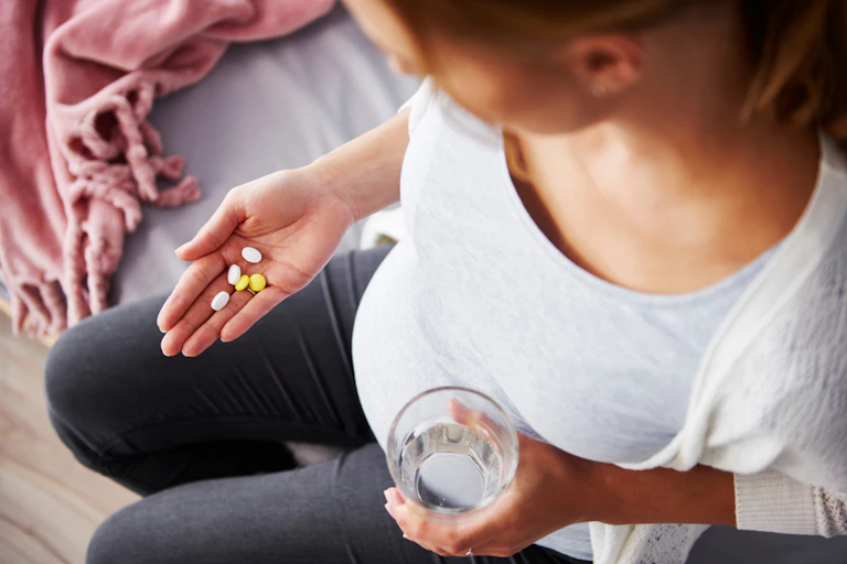 Pregnant woman holding glass water in one hand, supplements in other