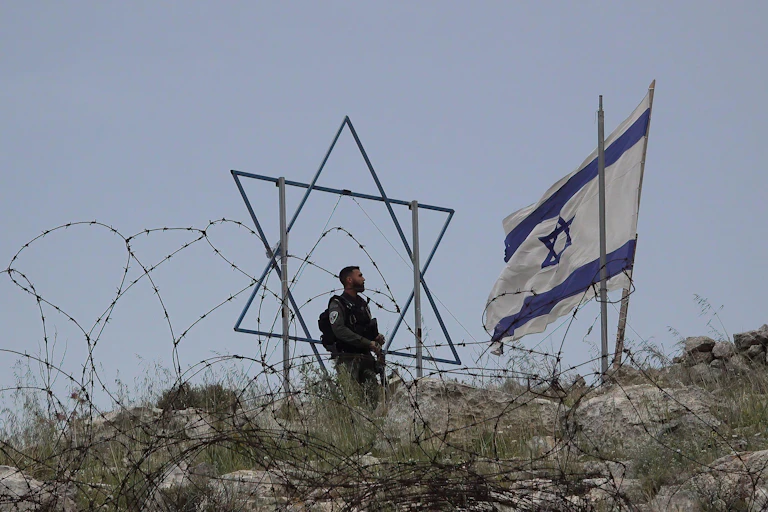 An IDF soldier stands next to a Star of David and Israeli flag.