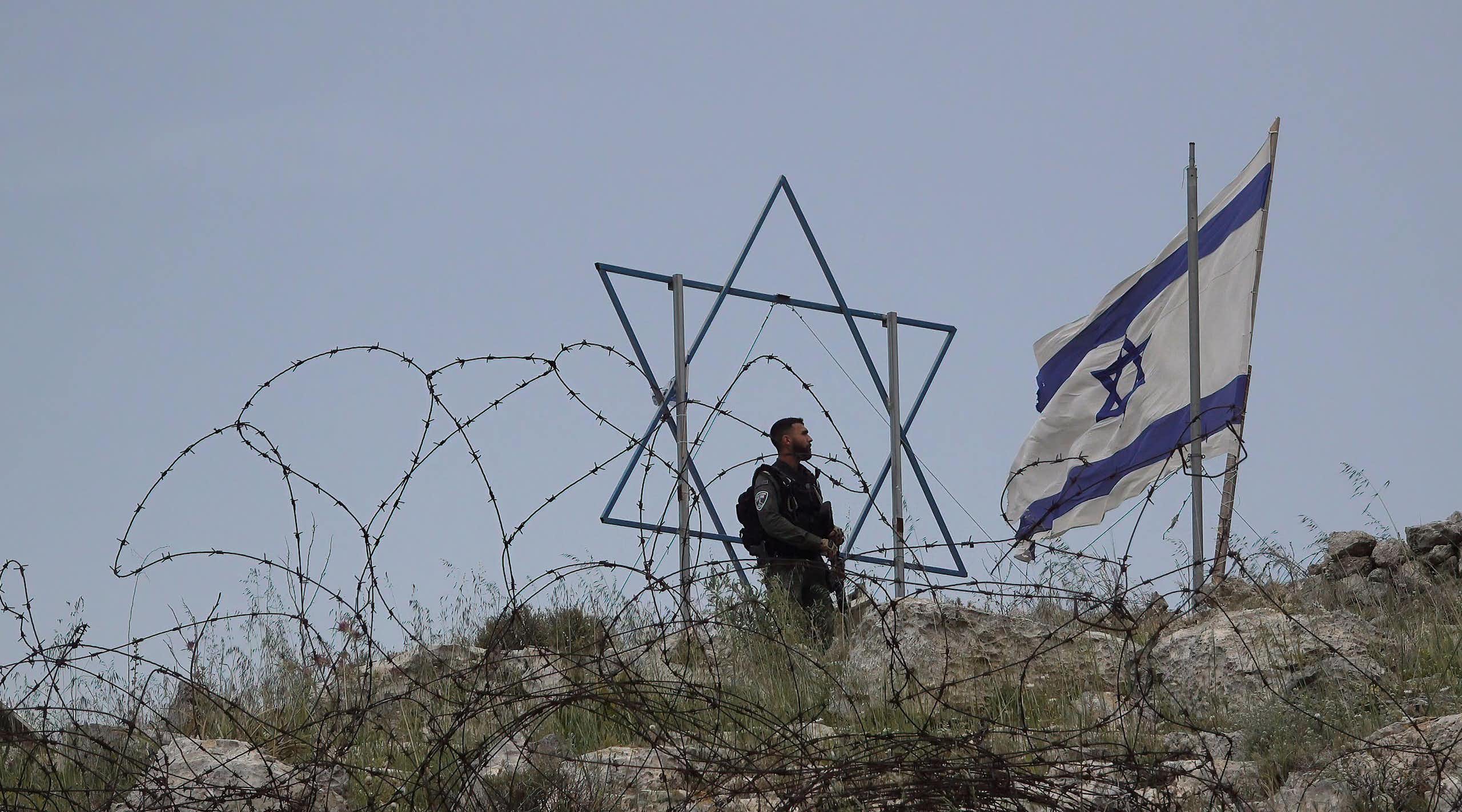 An IDF soldier stands next to a Star of David and Israeli flag.