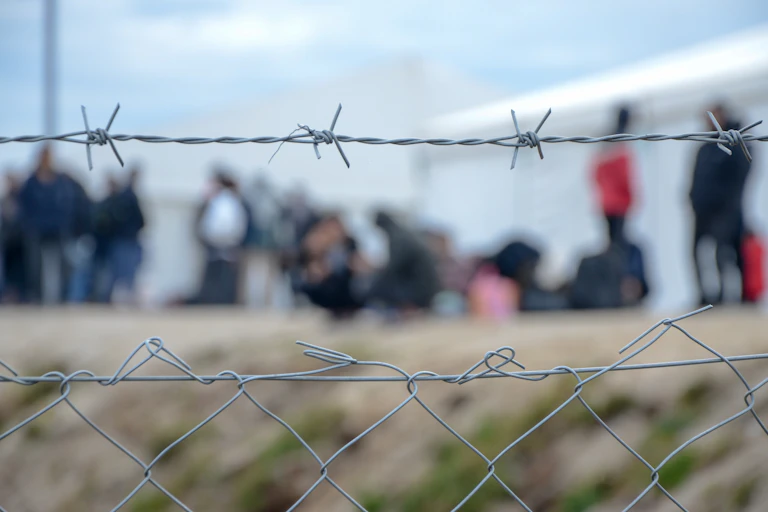 Barbed wire with a group of people in the background, out of focus