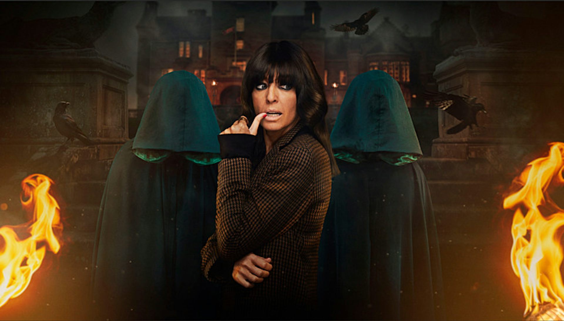 Claudia Winkleman stands in front of a spooky scene with flames on either side of her.