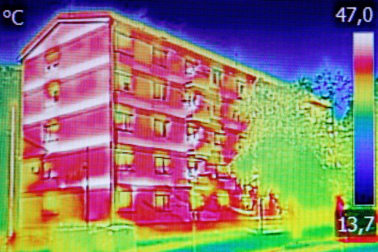 thermal imaging photo of residential block of flats in red, light green shape of tree to right, blue sky