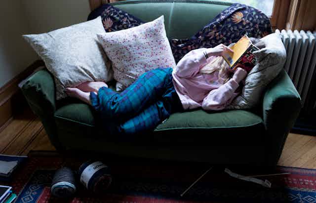 Young woman sprawled on couch covering her face with a book.