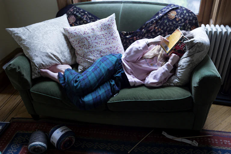 Young woman sprawled on couch covering her face with a book.