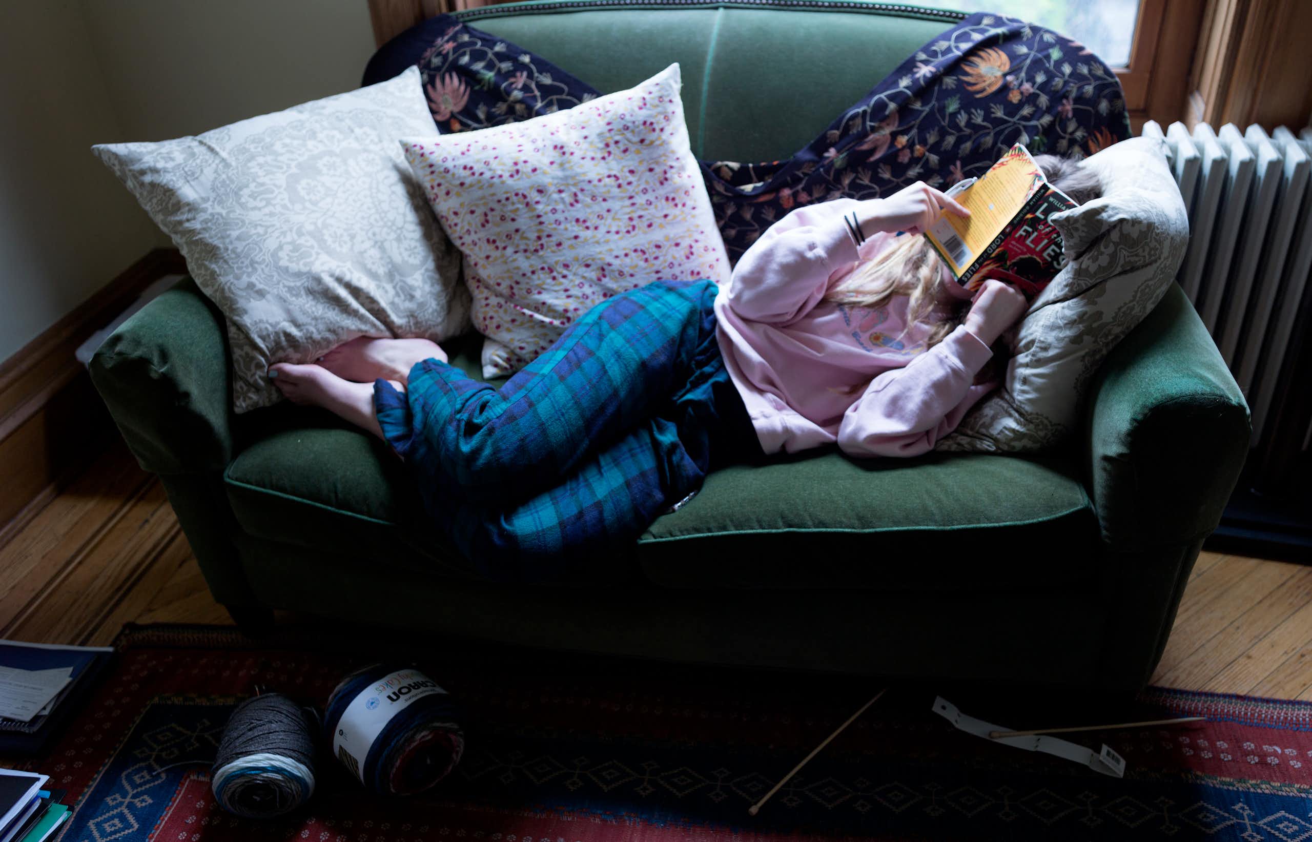 Young woman sprawled on couch covering her face with a book.
