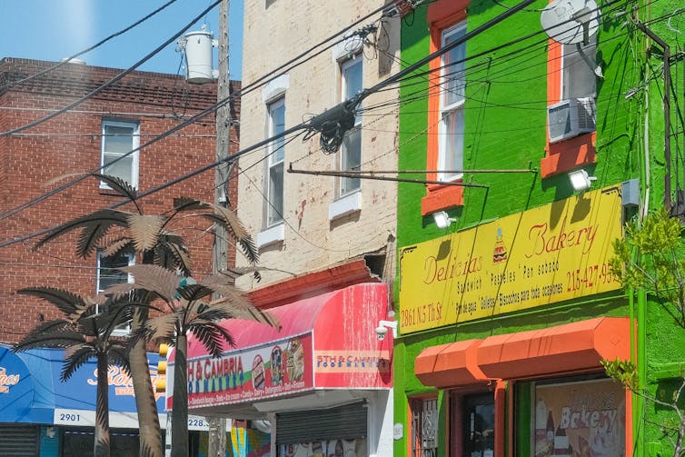 A street scene in North Philadelphia with colorful buildings and artificial palm trees.