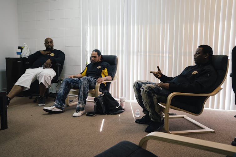 Three black men sit on chairs during a meeting to discuss reducing gun violence.
