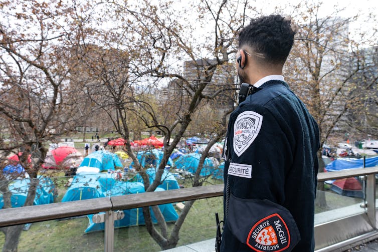 A uniformed security guard looks over an encampment of tents.
