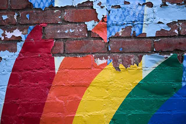 A painted rainbow peels off a brick wall.