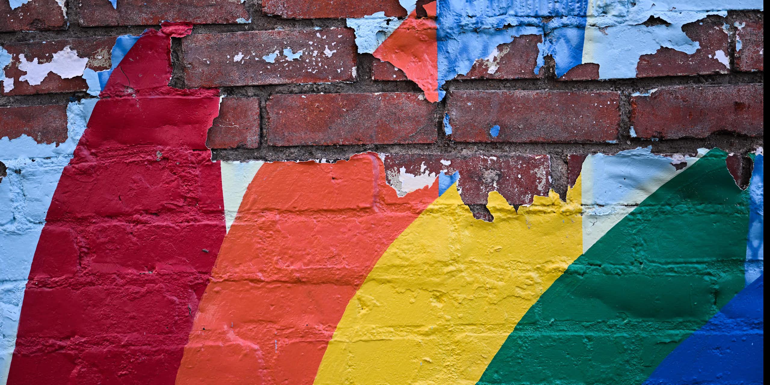 A painted rainbow peels off a brick wall.