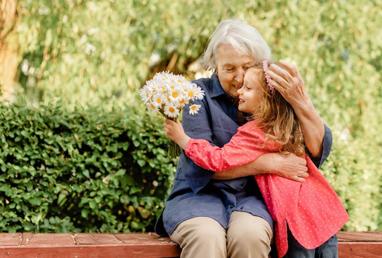 An eldery woman hugs a young girl carrying a bouquet of flowers