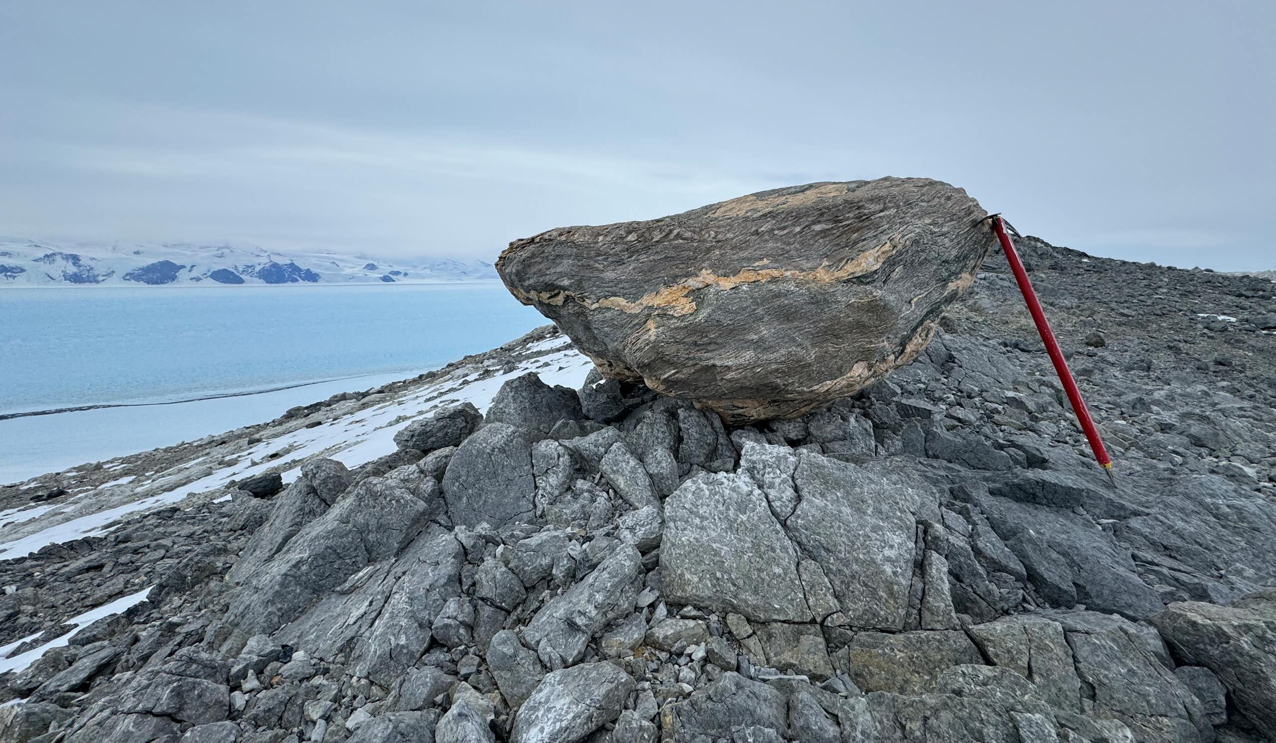 A rock perched on an outcrop in Antarctica, with am ice pick for size comparison.