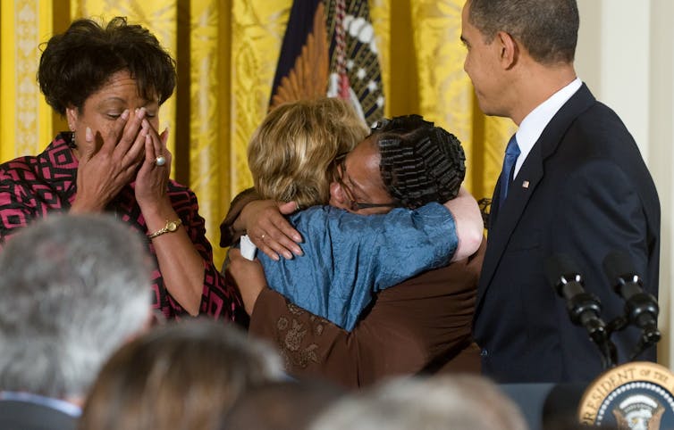 Four people at the front of a room, three of whom are in tears.