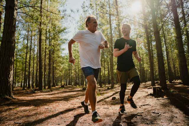 An older man and a younger man jogging happily in bushland.
