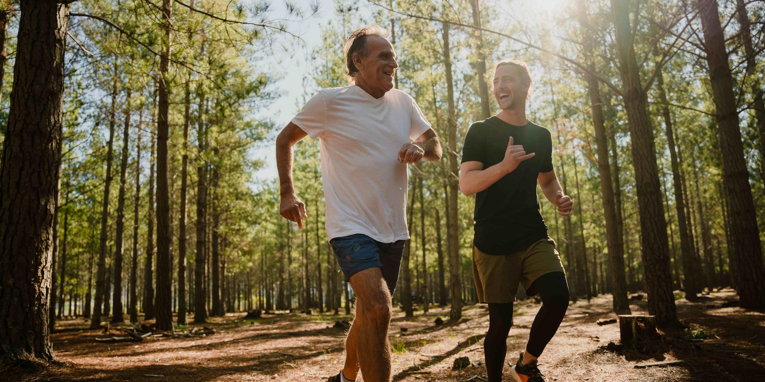 An older man and a younger man jogging happily in bushland.