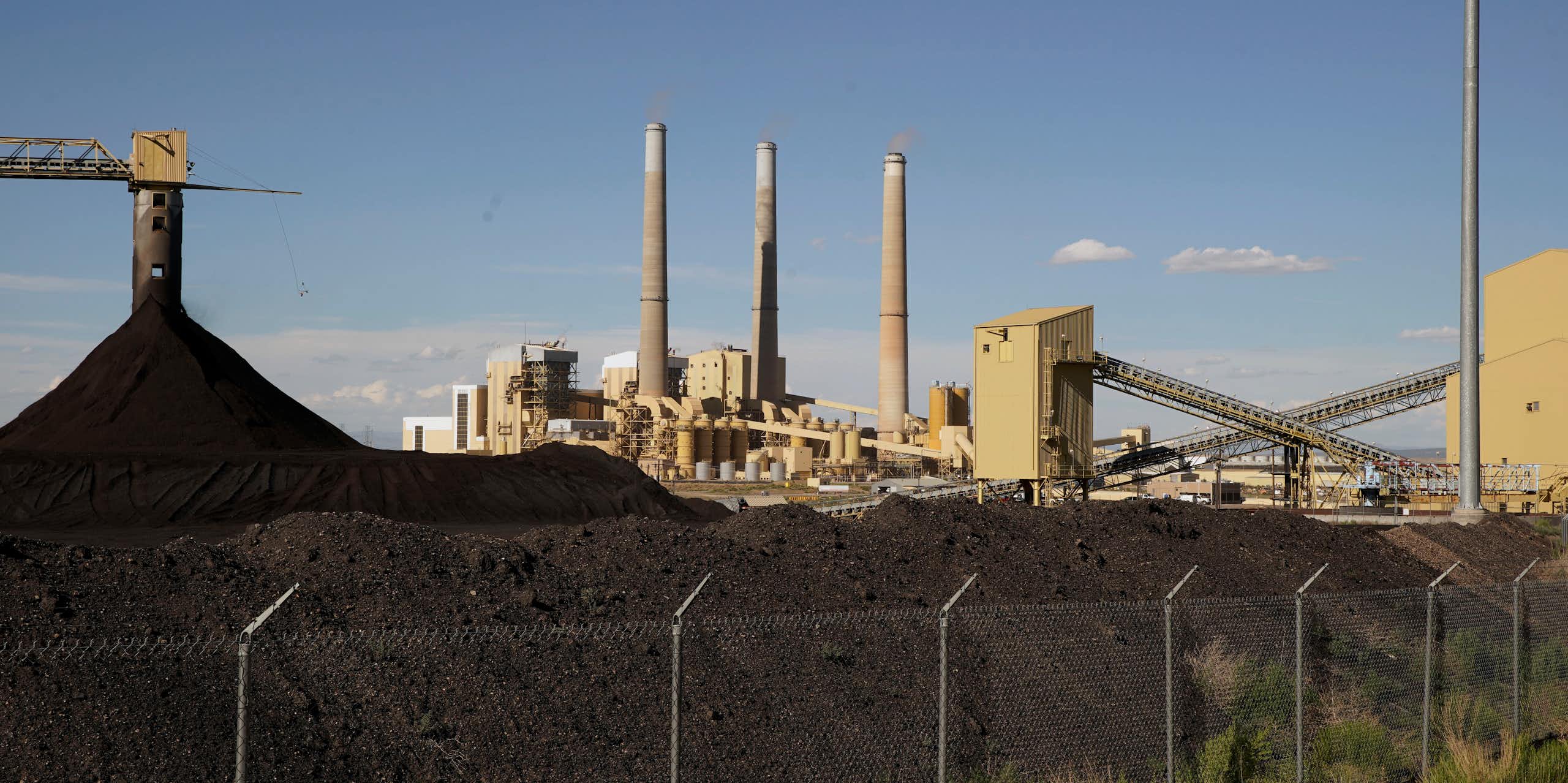 heaps of coal in front of a power plant with three tall smokestacks